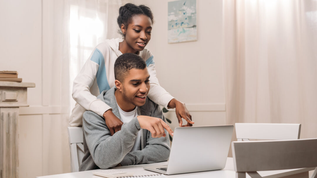 happy african american couple using laptop and pointing on screen at home