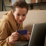 woman looking at a credit card while using her laptop