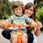 mom and toddler smiling and standing behind bike