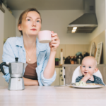 mom pondering and holding cup while baby eats next to her