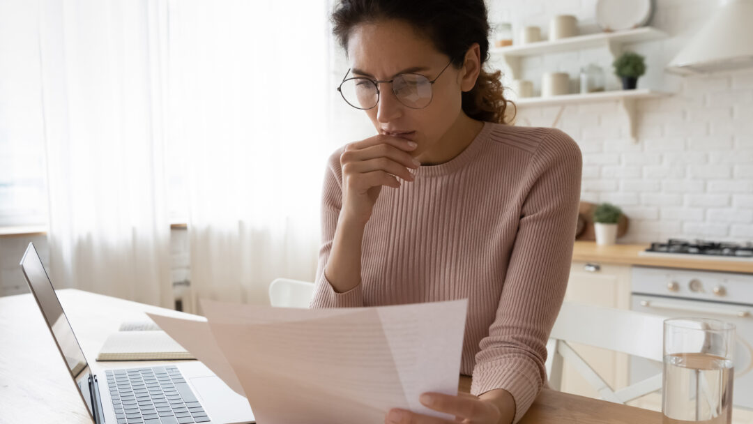 woman looking at computer and paper bills