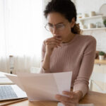 woman looking at computer and paper bills