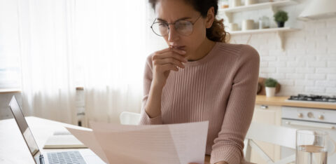 woman looking at computer and paper bills